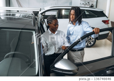 Doors are opened, looking inside. Car seller is assisting client in the automobile salon 136746646