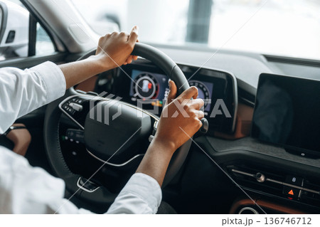 Two hands are on the steering wheel. Woman in white shirt is in the modern car 136746712