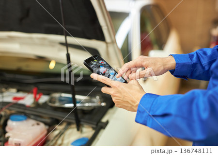 ボンネットの中をスマホで撮る自動車整備士 136748111