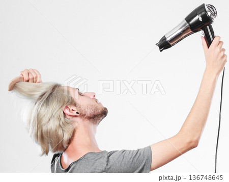 Young man drying hair with hairdryer 136748645