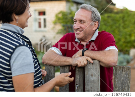 Elderly couple standing together near wooden fence in garden Elderly couple standing together near wooden fence in garden 136749433