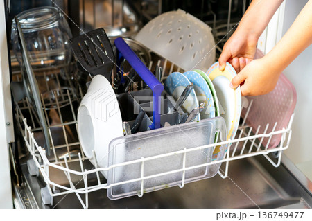 Children's hands load dirty dishes into the dishwasher Children's hands load dirty dishes into the dishwasher 136749477
