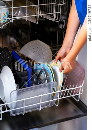 Children's hands load dirty dishes into the dishwasher 136749735