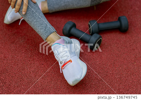 A girl rests on the sports ground after exercising with dumbbells A girl rests on the sports ground after exercising with dumbbells 136749745