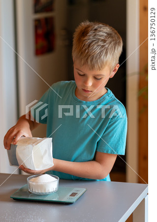 Boy weighing sugar from a pack on a kitchen scale Boy weighing sugar from a pack on a kitchen scale 136750129