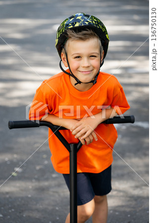 A young boy with blond hair and an orange T-shirt on a scooter 136750130