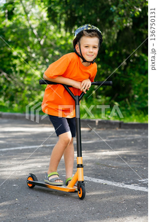 A young boy with blond hair and an orange T-shirt on a scooter A young boy with blond hair and an orange T-shirt on a scooter 136750131