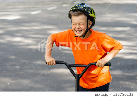 A young boy with blond hair and an orange T-shirt on a scooter 136750132