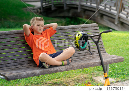 A young boy with blond hair and an orange T-shirt on a scooter A young boy with blond hair and an orange T-shirt on a scooter 136750134