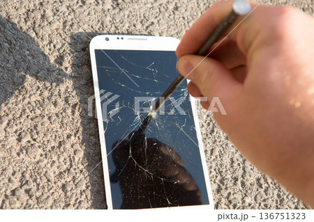 A hand drives a large metal nail through a smartphone screen with a hammer 136751323
