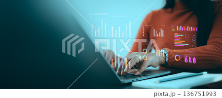 A professional business woman working on a laptop with holographic financial data charts and yearly summary analysis in a dark office. Ideal for fintech, big data, and digital marketing. A professional business woman working on a laptop with holographic financial data charts and yearly summary analysis in a dark office. Ideal for fintech, big data, and digital marketing. 136751993