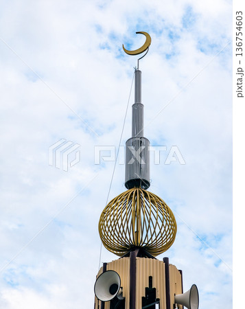 Islamic mosque minaret tower with golden crescent moon symbol and loudspeakers under blue sky and white clouds, religious architecture concept. Islamic mosque minaret tower with golden crescent moon symbol and loudspeakers under blue sky and white clouds, religious architecture concept. 136754603