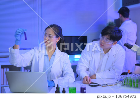 Two scientists review a purple liquid sample together in a modern laboratory, combining observation, data analysis, and collaborative research Two scientists review a purple liquid sample together in a modern laboratory, combining observation, data analysis, and collaborative research 136754972