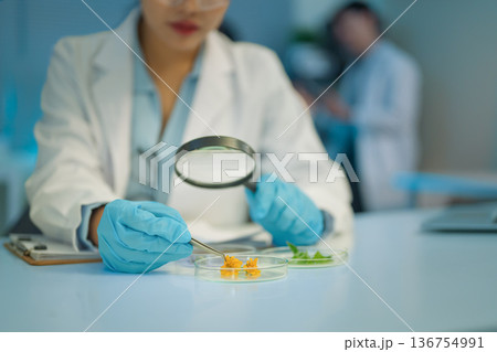 Scientist uses a magnifying glass to closely examine flower samples in petri dishes Scientist uses a magnifying glass to closely examine flower samples in petri dishes 136754991