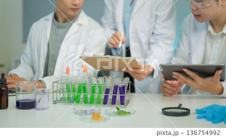 Cropped shot research team in lab coats analyzing test samples and recording data with laptop and tablet Cropped shot research team in lab coats analyzing test samples and recording data with laptop and tablet 136754992