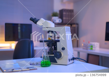 Laboratory workspace with microscope, green chemical solution, and research documents, representing modern scientific analysis and controlled experimentation. 136754999