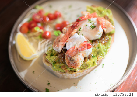 Open-faced toast topped with guacamole, shrimp, and poached eggs served with lemon and fresh garnish Open-faced toast topped with guacamole, shrimp, and poached eggs served with lemon and fresh garnish 136755321