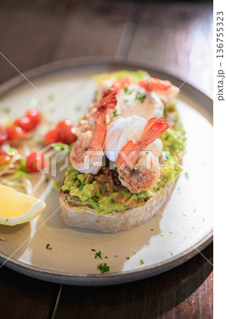 Open-faced toast topped with guacamole, shrimp, and poached eggs served with lemon and fresh garnish Open-faced toast topped with guacamole, shrimp, and poached eggs served with lemon and fresh garnish 136755323