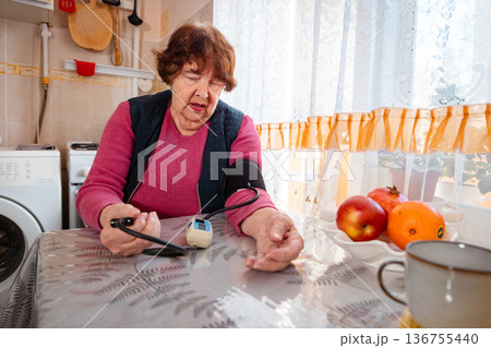Elderly Caucasian woman monitors blood pressure indoors during a routine check. She focuses on self care and healthy aging. Concept of active senior lifestyle and disease prevention. Elderly Caucasian woman monitors blood pressure indoors during a routine check. She focuses on self care and healthy aging. Concept of active senior lifestyle and disease prevention. 136755440