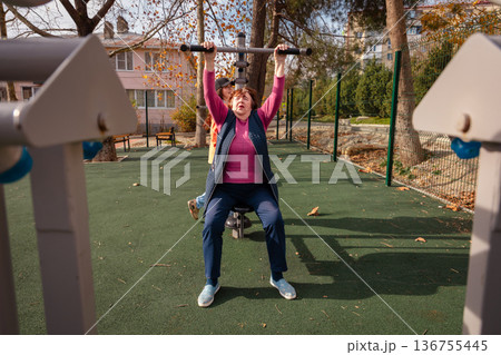 Elderly Caucasian woman training on a street gym in an urban park. Sport, wellness, and active senior lifestyle concept. Elderly Caucasian woman training on a street gym in an urban park. Sport, wellness, and active senior lifestyle concept. 136755445