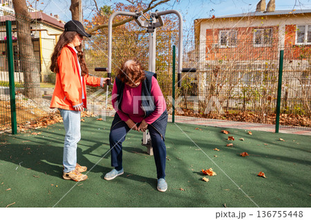Elderly Caucasian woman works with a personal trainer on outdoor equipment. Physical activity improves mobility, health, and long term recovery. Elderly Caucasian woman works with a personal trainer on outdoor equipment. Physical activity improves mobility, health, and long term recovery. 136755448