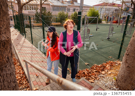 Mature grandmother walking hand in hand with her granddaughter in a sunny park. Outdoor enjoyment and senior lifestyle. 136755455