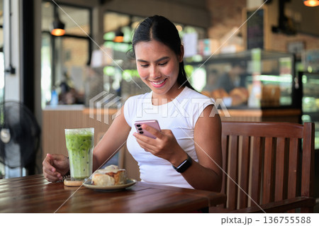 Smiling Woman Using Smartphone in Cafe with Green Iced Tea Matcha Latte Drink and Dessert Smiling Woman Using Smartphone in Cafe with Green Iced Tea Matcha Latte Drink and Dessert 136755588