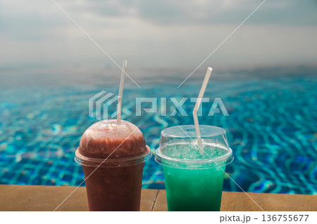 Two chilled drinks on infinity pool edge with blue water and soft sky creating tropical vacation refreshment scene and clean background for resort and travel concepts 136755677