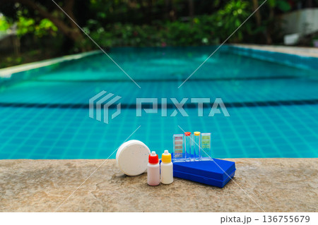 Pool water testing kit with chlorine tablet and reagent bottles on stone edge, tropical swimming pool background Pool water testing kit with chlorine tablet and reagent bottles on stone edge, tropical swimming pool background 136755679