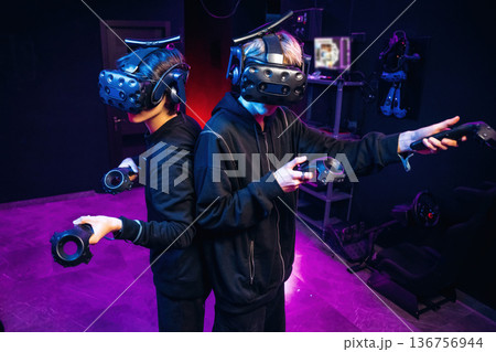 Doing hands gestures. Two young men in virtual reality glasses indoors Doing hands gestures. Two young men in virtual reality glasses indoors 136756944