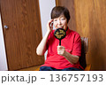 室内に座って、手鏡で顔を見ながらこめかみに手を当てるシニア女性 136757193