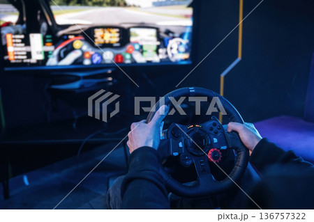 Using steering wheel. Young guy is playing racing game by using driving simulator Using steering wheel. Young guy is playing racing game by using driving simulator 136757322