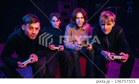 Looking forward, playing together. Young gamers are with console controllers indoors Looking forward, playing together. Young gamers are with console controllers indoors 136757355