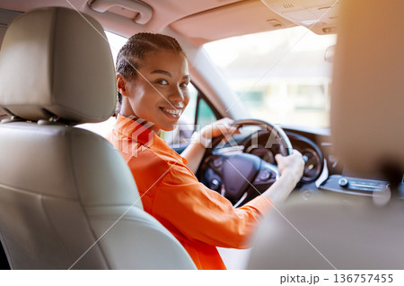 Black woman turning back from driver seat and smiling warmly at passenger 136757455