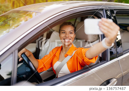 Young black woman taking selfie inside car while driving, capturing joyful moment Young black woman taking selfie inside car while driving, capturing joyful moment 136757487