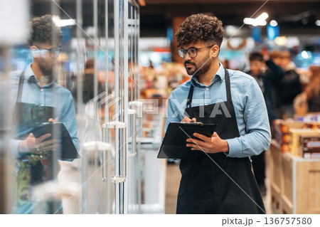 With notepad. Male worker is in the grocery store With notepad. Male worker is in the grocery store 136757580