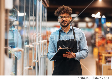 Black notepad in hands. Male worker is in the grocery store 136757583