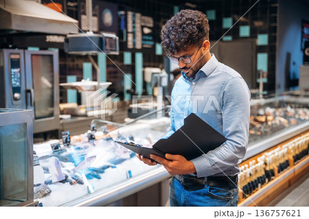 Black notepad in hands. Male worker is in the grocery store Black notepad in hands. Male worker is in the grocery store 136757621