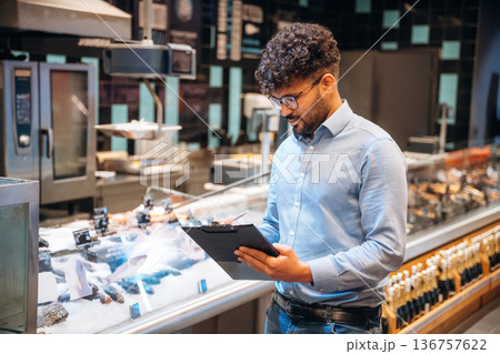 Black notepad in hands. Male worker is in the grocery store 136757622