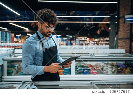 Manager is with notepad. Male worker is in the grocery store 136757637