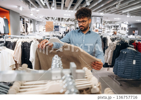 Holding the sweater. Man customer is in the clothing store 136757716