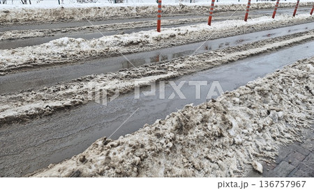 Dirty snow and slush on city road with puddle and traffic posts in winter. Urban weather and transportation safety concept 136757967