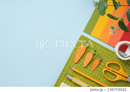 Items for paper art hobby: scissors, pencil, eraser, cutting mat on blue background. Paper carrots. Space for your text. Items for paper art hobby: scissors, pencil, eraser, cutting mat on blue background. Paper carrots. Space for your text. 136758082