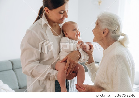Enjoying of being together. Mother, grandmother and little baby child on hands indoors 136758246