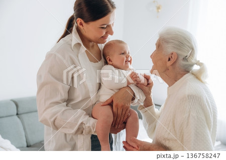 Standing, looking at each other. Mother, grandmother and little baby child on hands indoors 136758247