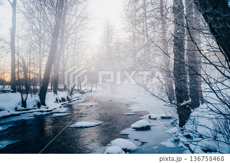 Misty winter forest river with snow and ice at dawn, tranquil Nordic nature scene Misty winter forest river with snow and ice at dawn, tranquil Nordic nature scene 136758468