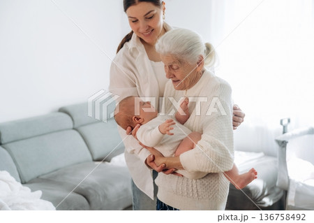 Cheerful facial expression. Mother, grandmother and little baby child on hands indoors 136758492
