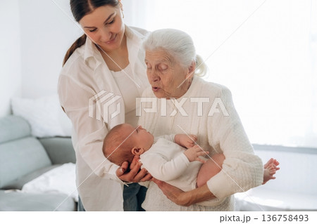 Feeling cute, holding toddler. Mother, grandmother and little baby child on hands indoors Feeling cute, holding toddler. Mother, grandmother and little baby child on hands indoors 136758493