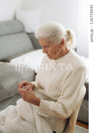 Grandma sits in a chair at home and knits clothes Grandma sits in a chair at home and knits clothes 136758642