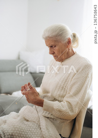 Grandma sits in a chair at home and knits clothes Grandma sits in a chair at home and knits clothes 136758643